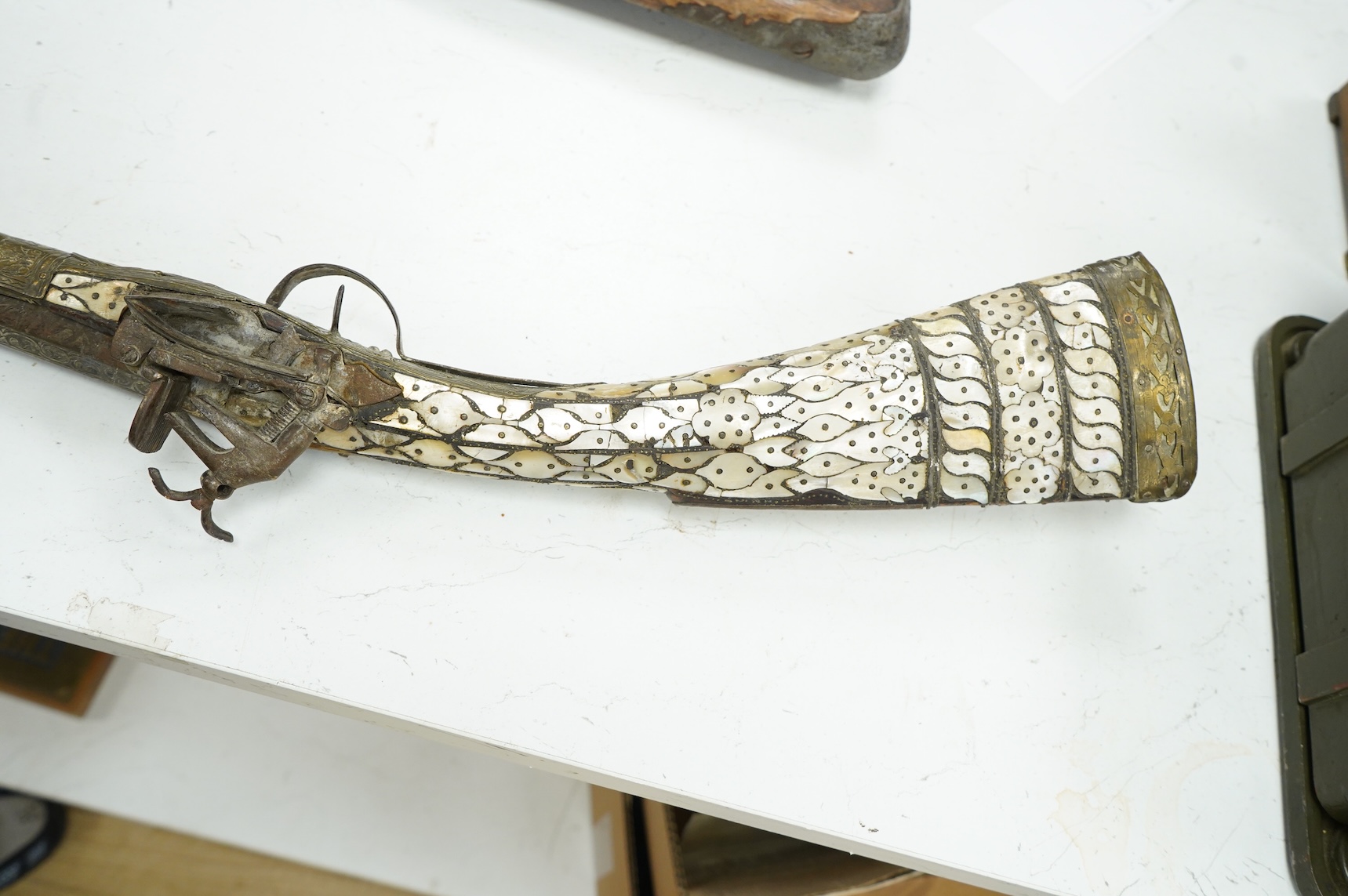 A Balkan miquelet flintlock gun with part octagonal Damascus twist barrel, silver inlaid at breach and muzzle, brass covered stock with shaped mother-of-pearl segments covering the butt, the side of stock inscribed ‘Piet